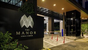 L'ingresso di un hotel con insegna moderna, vialetto recintato e area verde curata.