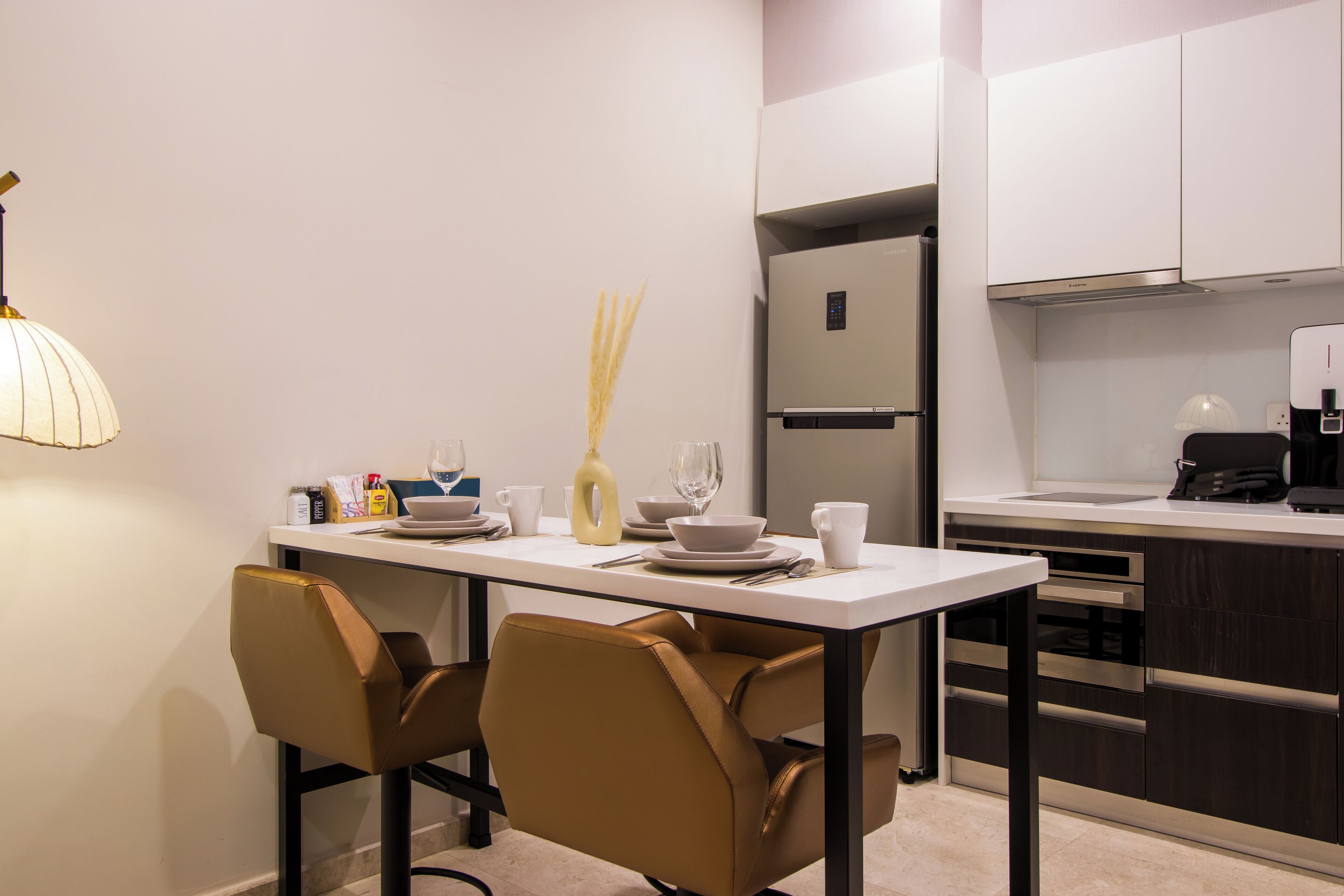 Una cocina moderna con encimera blanca, electrodomésticos de acero inoxidable y un comedor con dos sillas y una mesa.