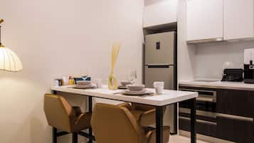 Una cocina moderna con encimera blanca, electrodomésticos de acero inoxidable y un comedor con dos sillas y una mesa.