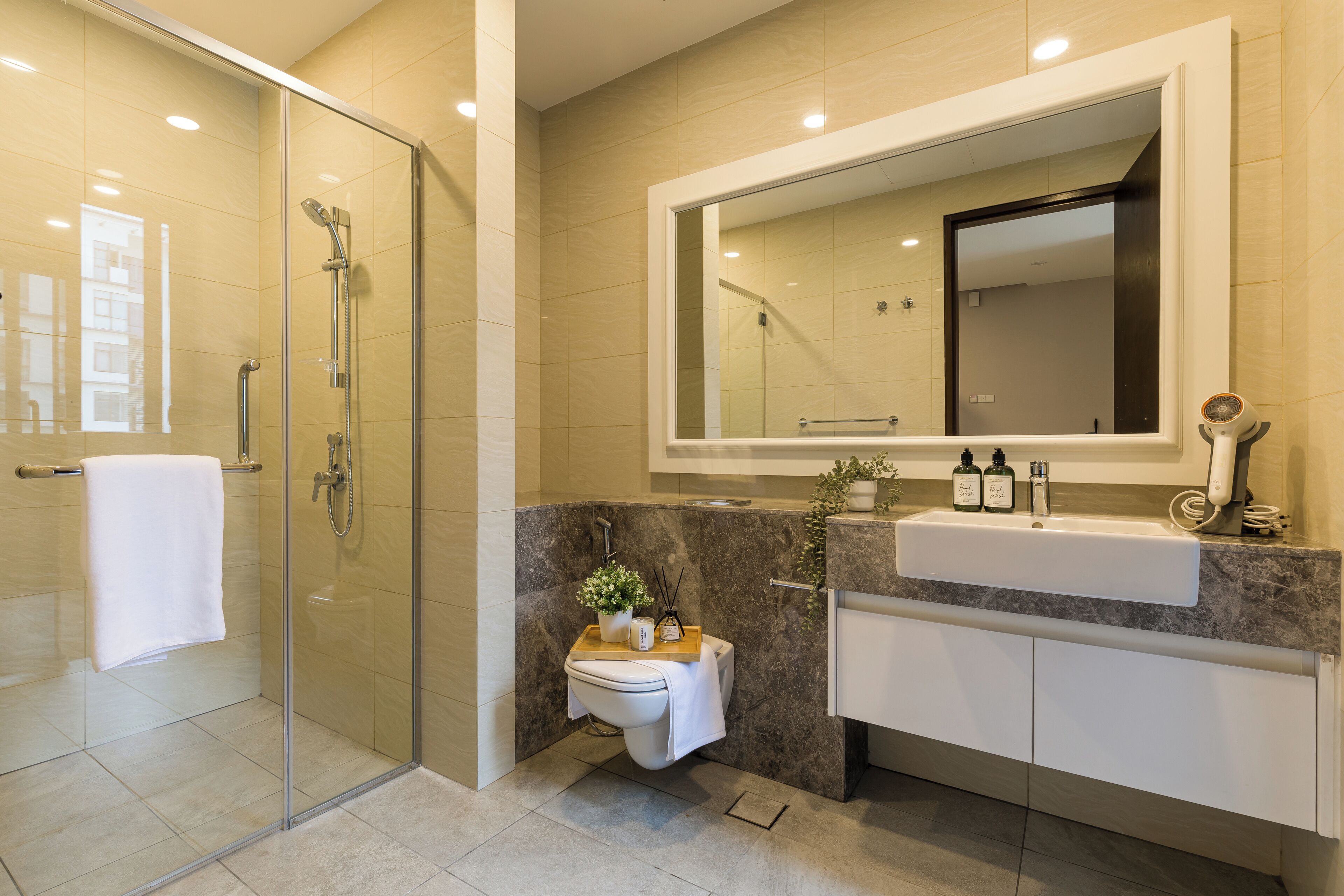 A modern bathroom with a glass-enclosed shower, a vanity with a large mirror, and a small toilet with a towel and decorative items.