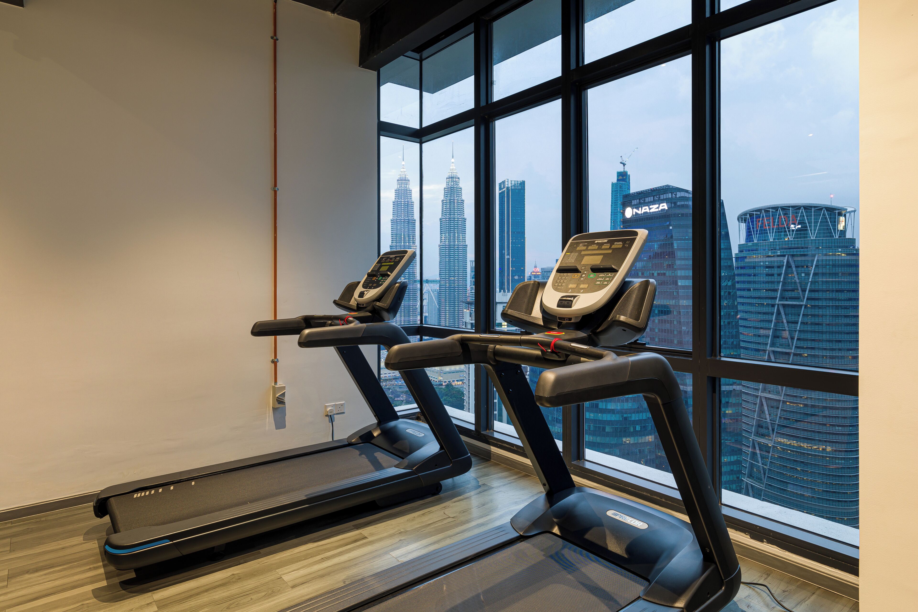 A gym with treadmills and a stationary bike, large windows with a cityscape view.
