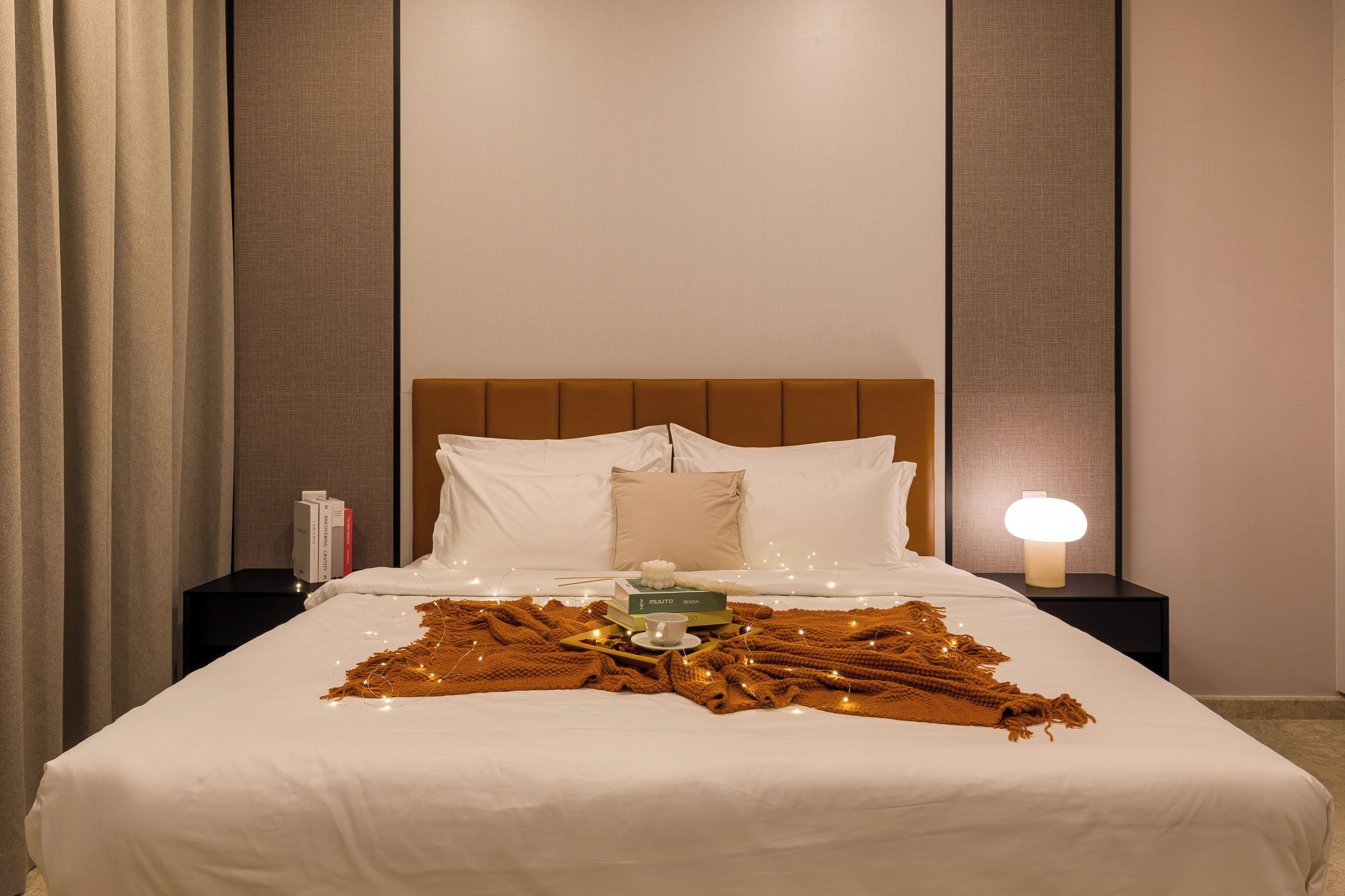 A neatly made bed with a white comforter, a brown throw blanket, and a bedside table with a lamp and books.