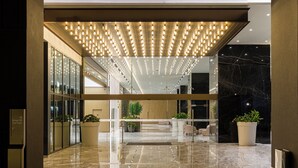 Una hall moderna con pavimento in marmo lucido, ingresso in vetro e soffitto illuminato da faretti lineari.