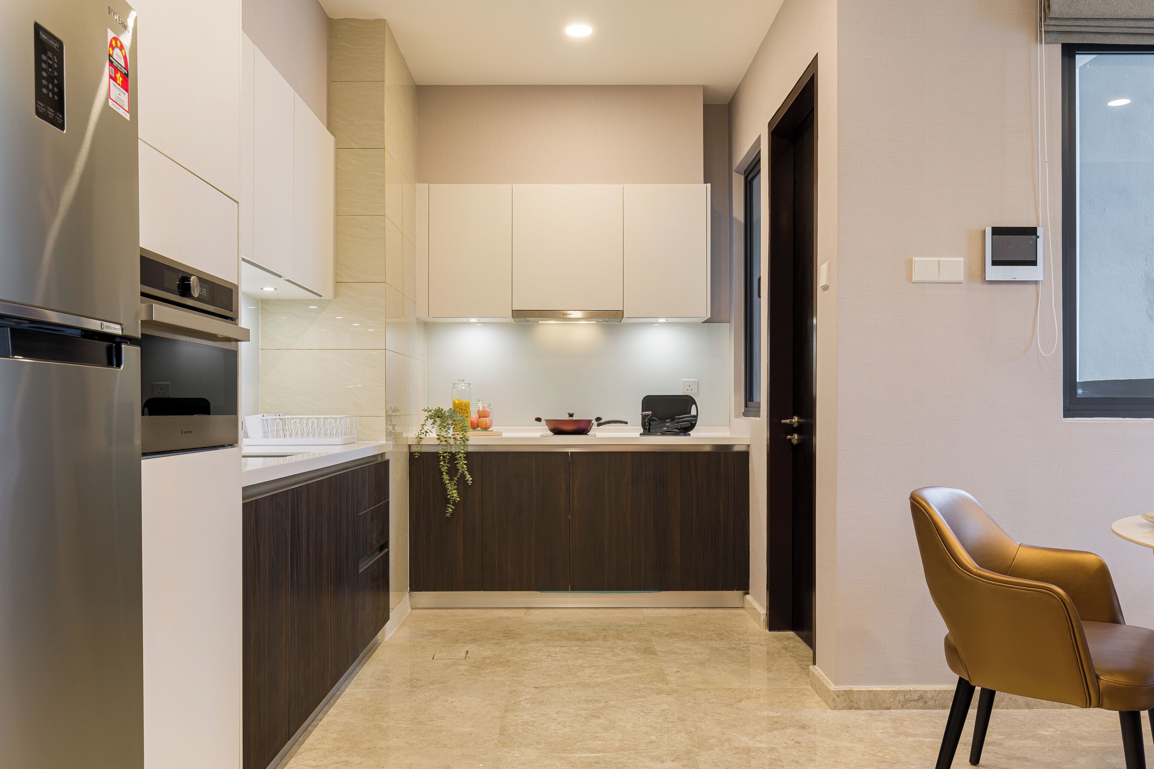 A modern kitchen with a built-in oven, a refrigerator, and a dining area with a chair.