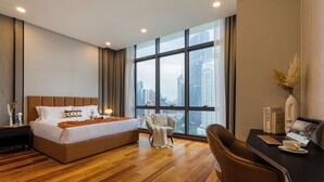 Camera d'albergo moderna con un letto grande, una scrivania con un portatile e vista sulla città attraverso ampie finestre.