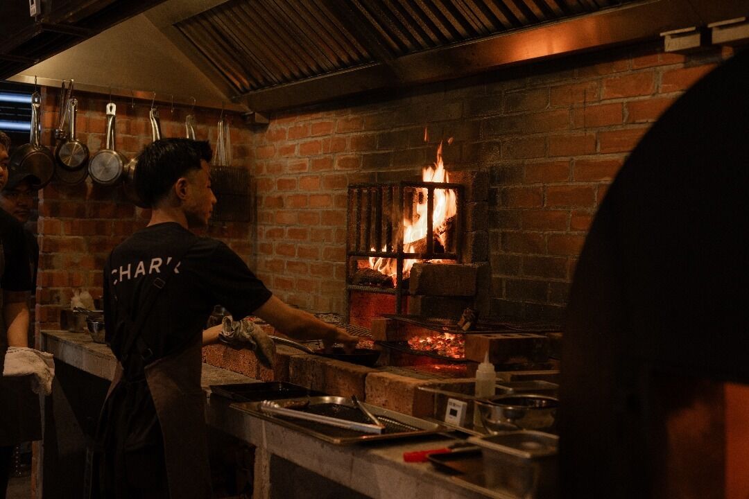 A chef working in a brick oven kitchen with a fire burning inside.