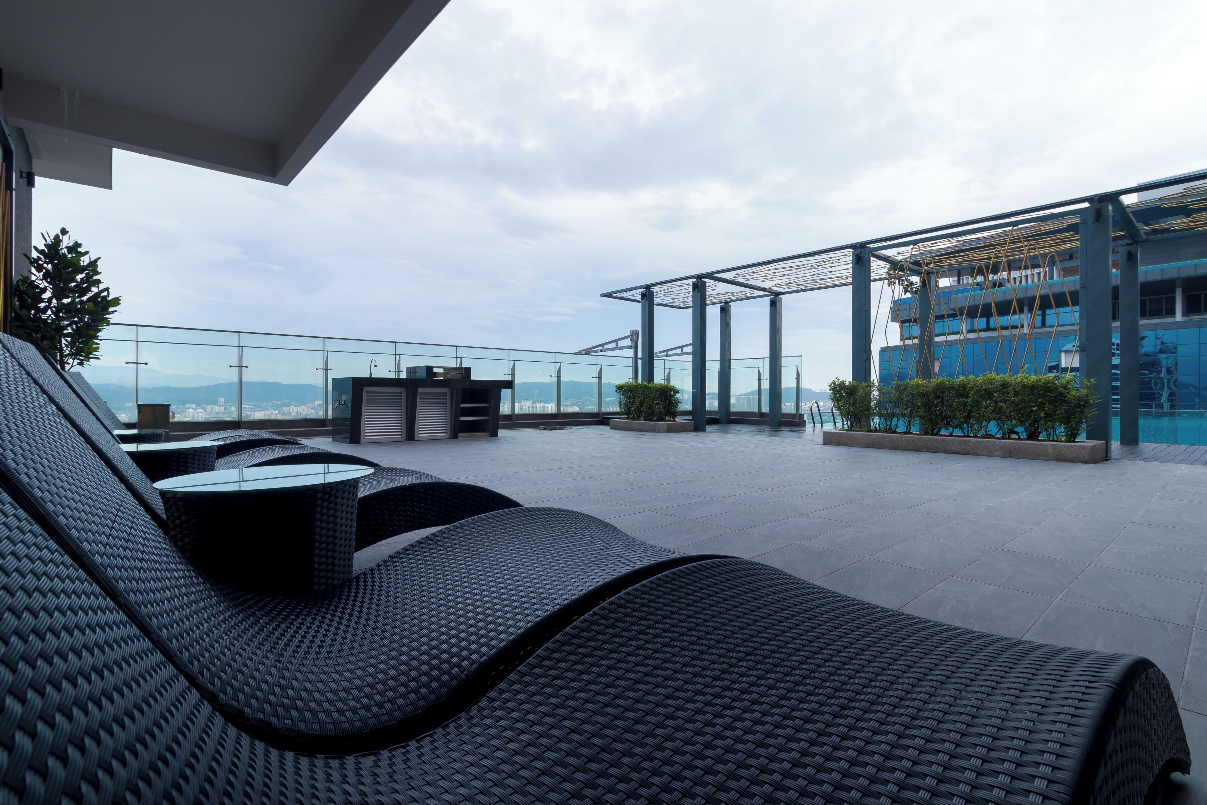Une terrasse sur le toit, aménagée avec des meubles en osier, une table en verre et offrant une vue sur un immeuble moderne et des montagnes.
