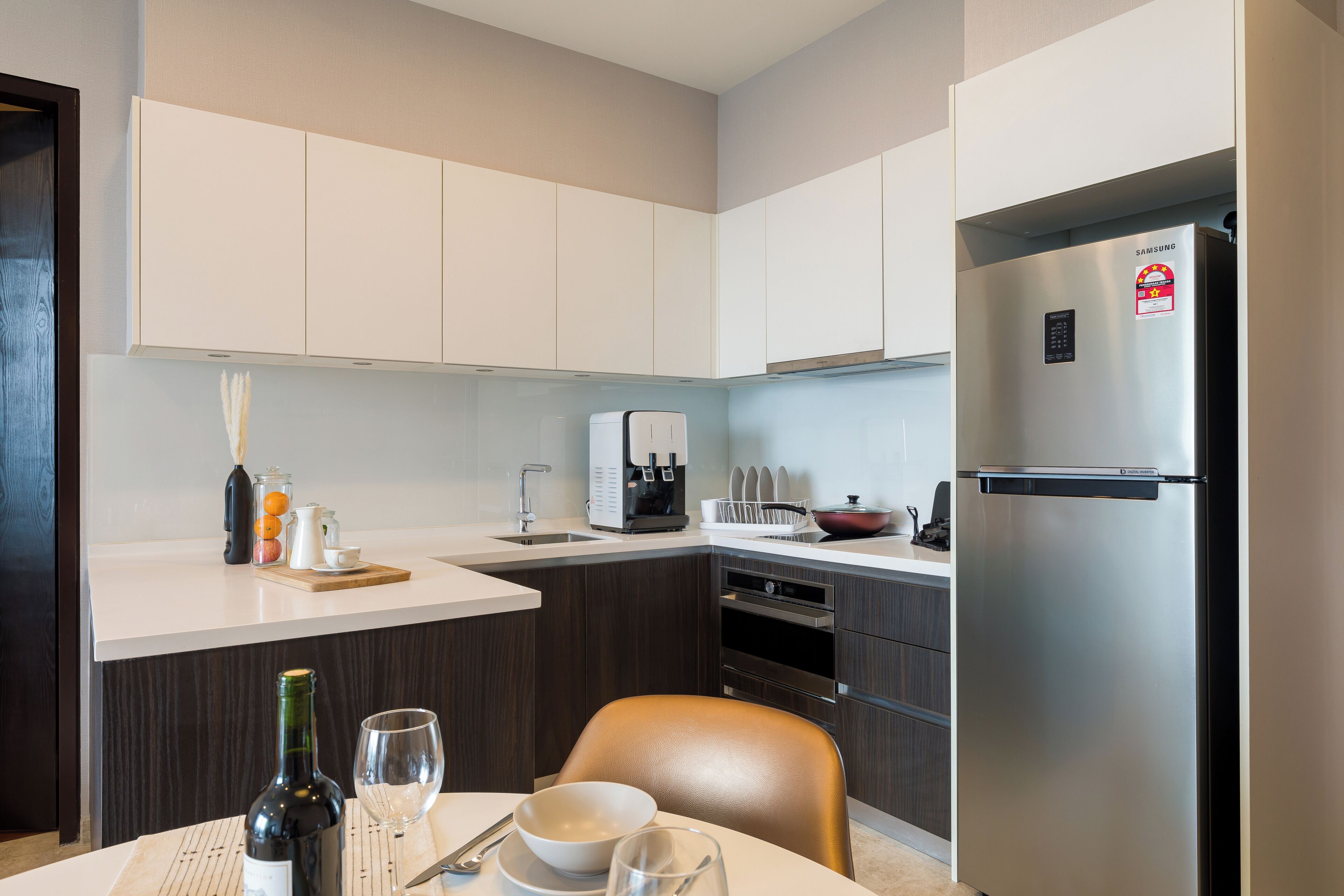 Une cuisine moderne avec des meubles blancs, un réfrigérateur en acier inoxydable et un coin repas avec une table dressée pour deux personnes.