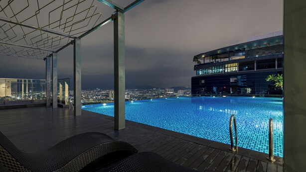 Una piscina a sfioro con vista sulla città, sedie a sdraio e un edificio moderno sullo sfondo.