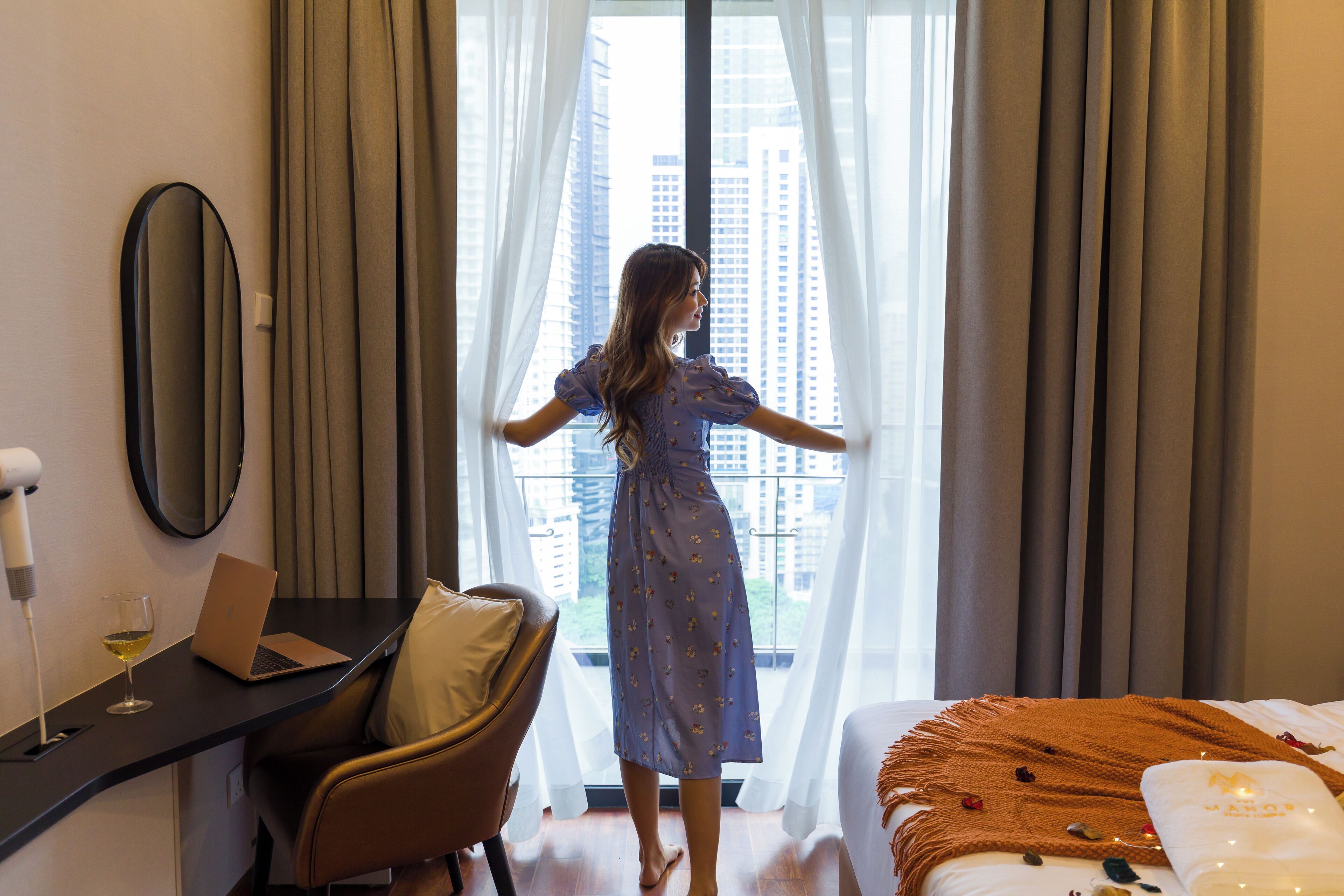 Una habitación de hotel con una cama, un escritorio con una computadora portátil, una silla y una ventana con cortinas.