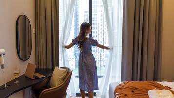A hotel room with a bed, a desk with a laptop, a chair, and a window with curtains.