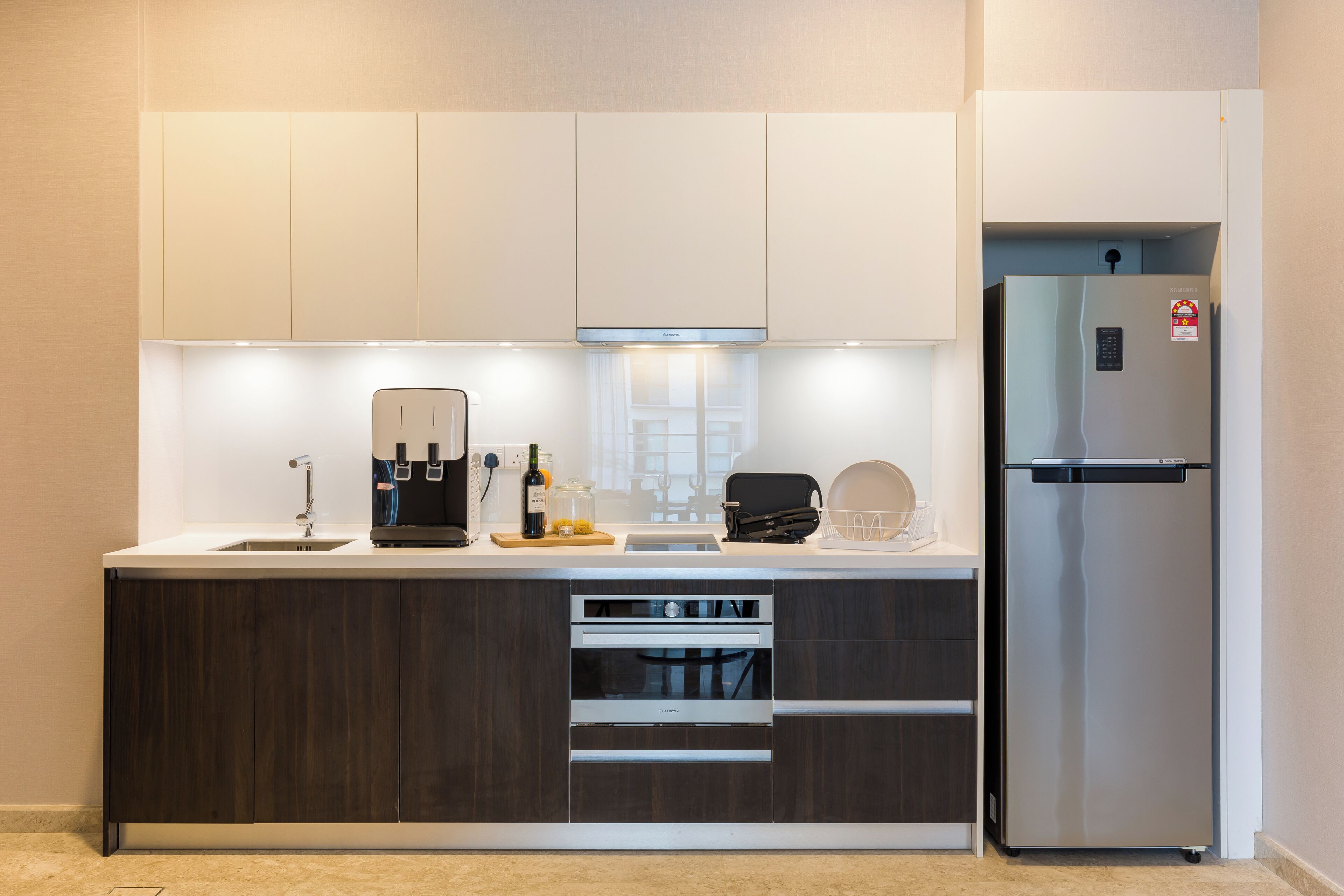 Una cocina moderna con armarios de madera oscura, horno empotrado, refrigerador de acero inoxidable y cafetera.