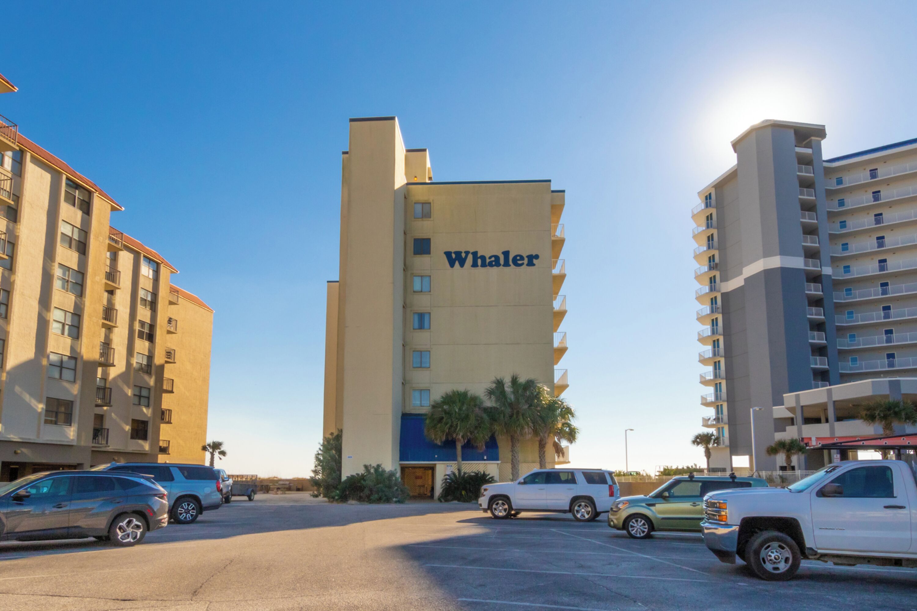 A hotel named Whaler with multiple floors, a parking lot with several cars, and palm trees in the foreground.