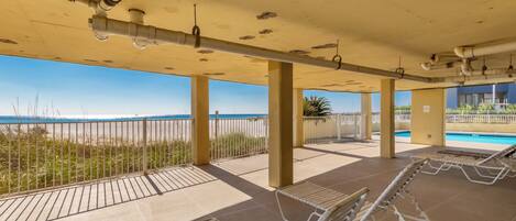 Un espace extérieur abrité, doté de chaises longues, d’une piscine et offrant une vue sur la plage.