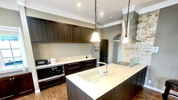 A modern kitchen with dark wooden cabinets, a white countertop, and a large island with a sink. - Villa Sapporo Seiga (Sapporo)