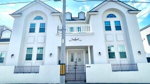 A two-story white building with a central entrance, a balcony, and a gated driveway. - Villa Sapporo Seiga (Sapporo)