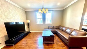 A living room with a flat-screen TV, a leather sofa, a wooden coffee table, and a chandelier. - Villa Sapporo Seiga (Sapporo)