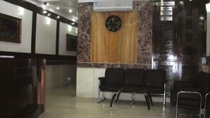A reception area with a clock, a reception desk, and several black chairs arranged for waiting. - National Lodge (New Delhi)