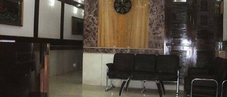 A reception area with a clock, a reception desk, and several black chairs arranged for waiting.