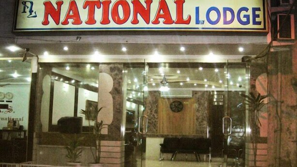The exterior of the National Lodge with a prominent sign, glass doors, and a bench outside. - National Lodge (New Delhi)