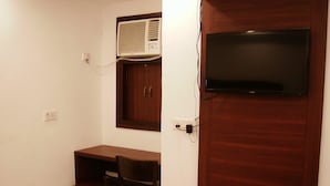 A small room with a wooden desk, a chair, a television mounted on a wooden wall, and an air conditioning unit above the desk. - National Lodge (New Delhi)