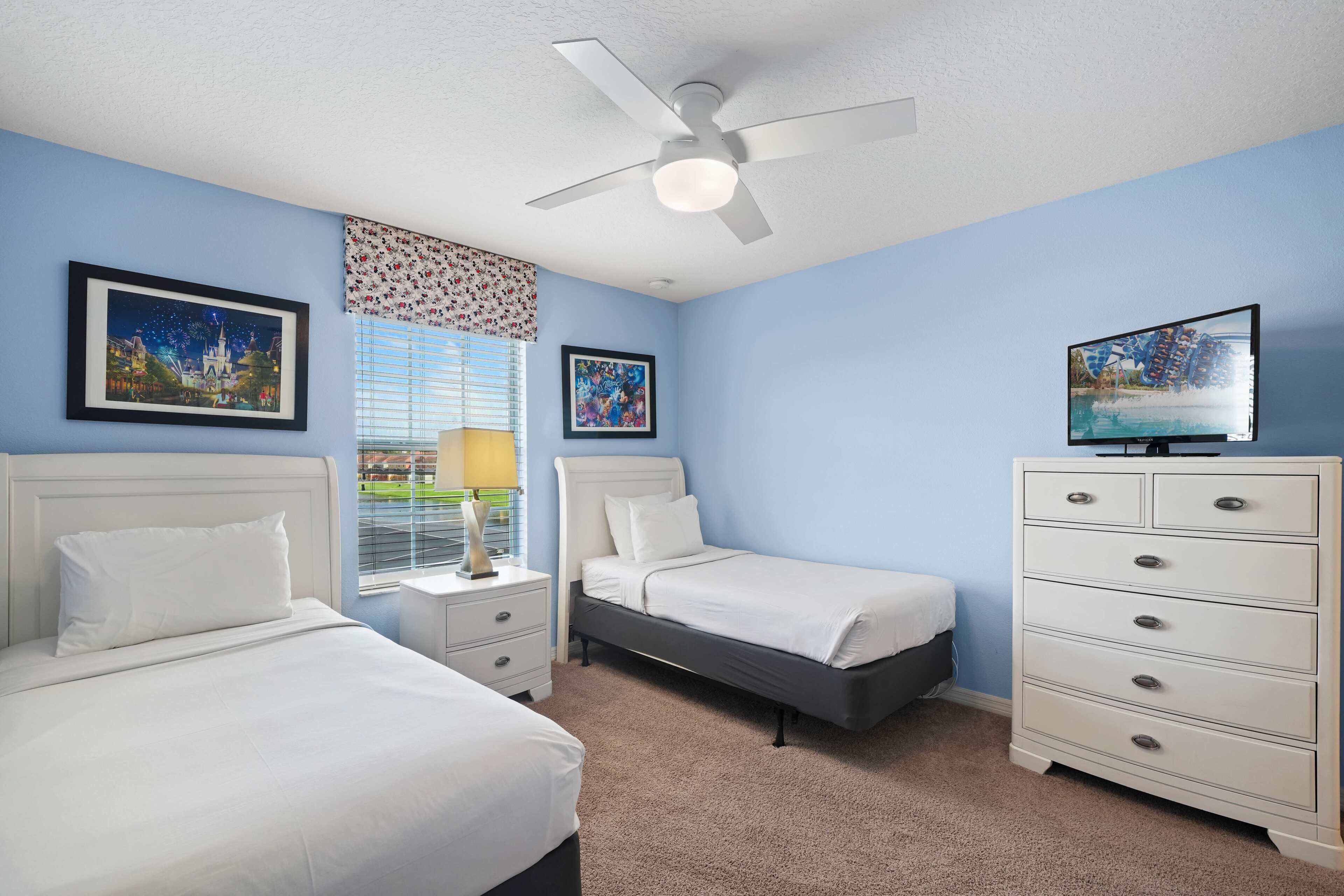 A bedroom with two beds, a dresser, a ceiling fan, and a TV.