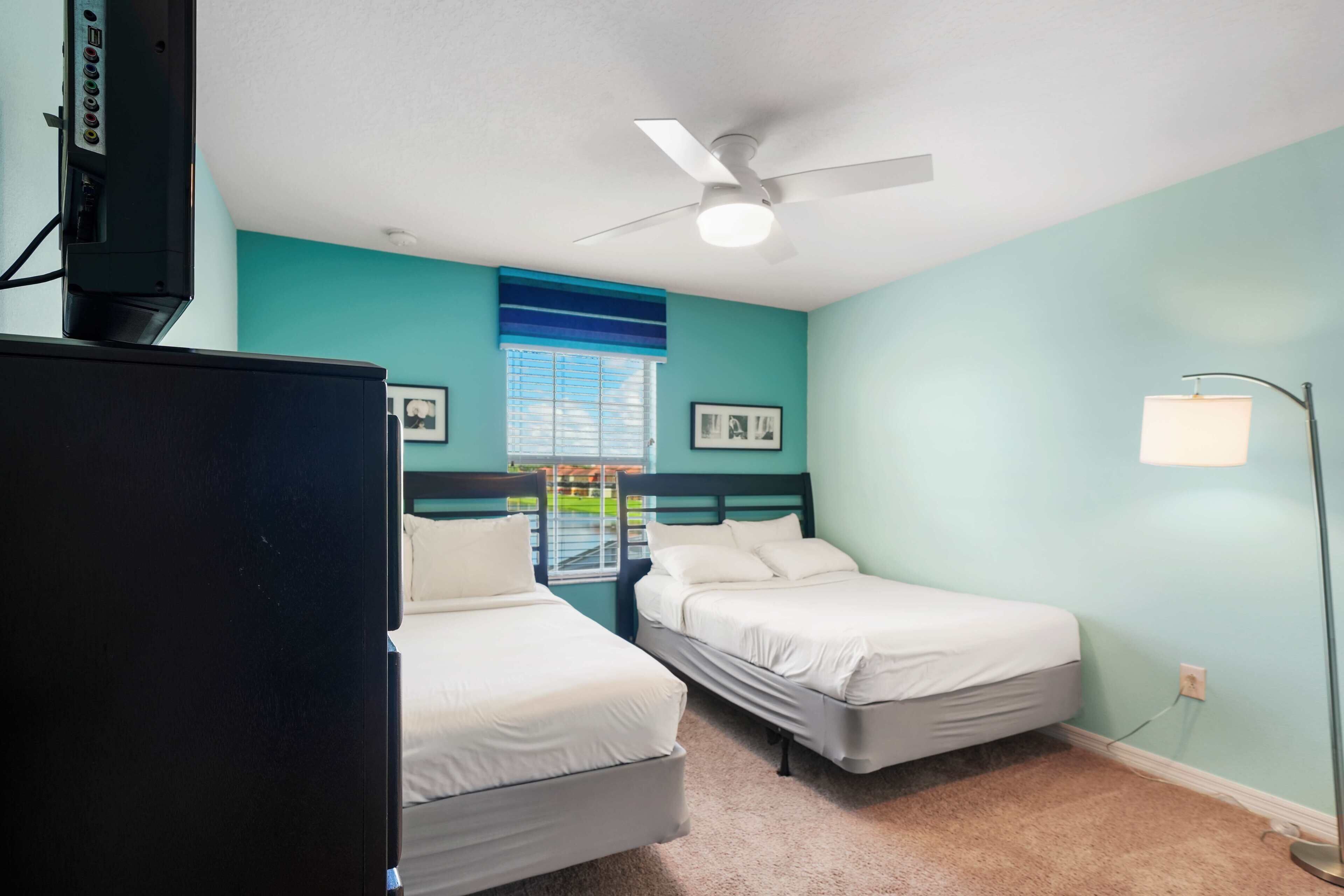 A room with two beds, a ceiling fan, a TV, and a window with blinds.