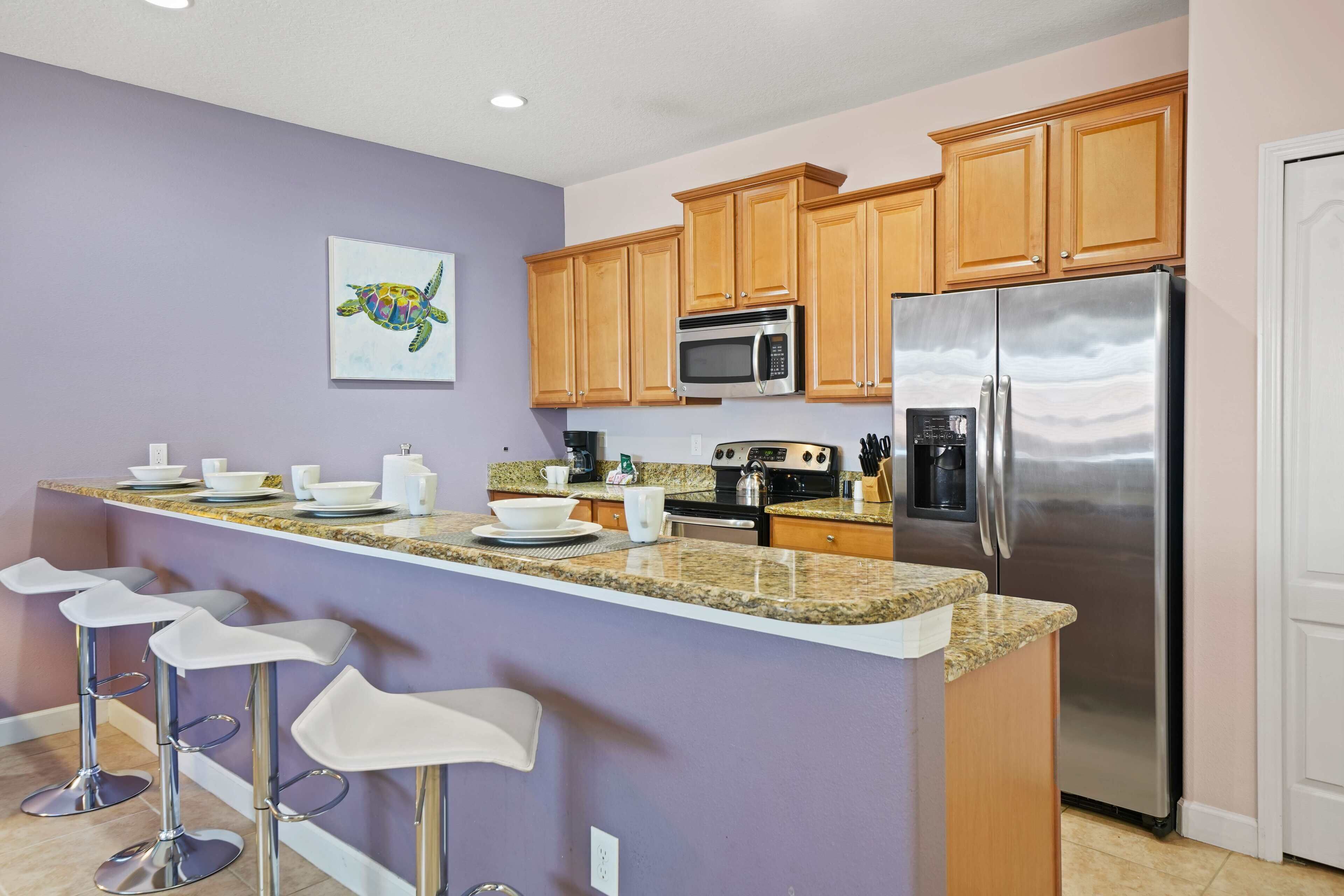 A kitchen with wooden cabinets, a stainless steel refrigerator, a granite countertop, and a bar stool area.