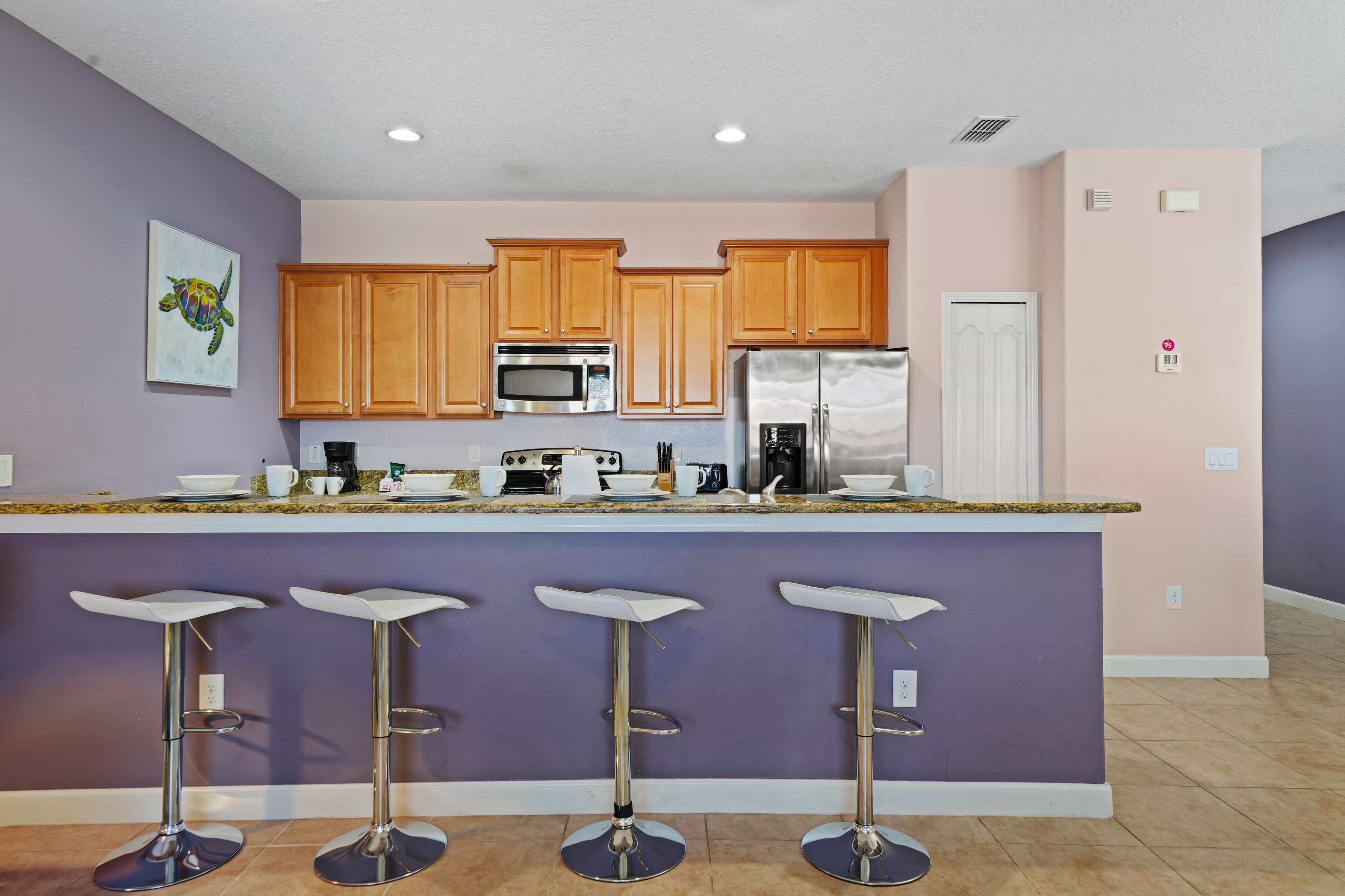 A kitchen with wooden cabinets, a stainless steel refrigerator, a microwave, and a coffee maker. There are four bar stools at the island.