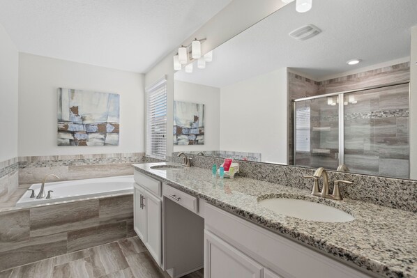 A modern bathroom with a large freestanding bathtub, a double sink vanity, and a large mirror. - 4718 Sleepy Hollow Drive (Kissimmee)