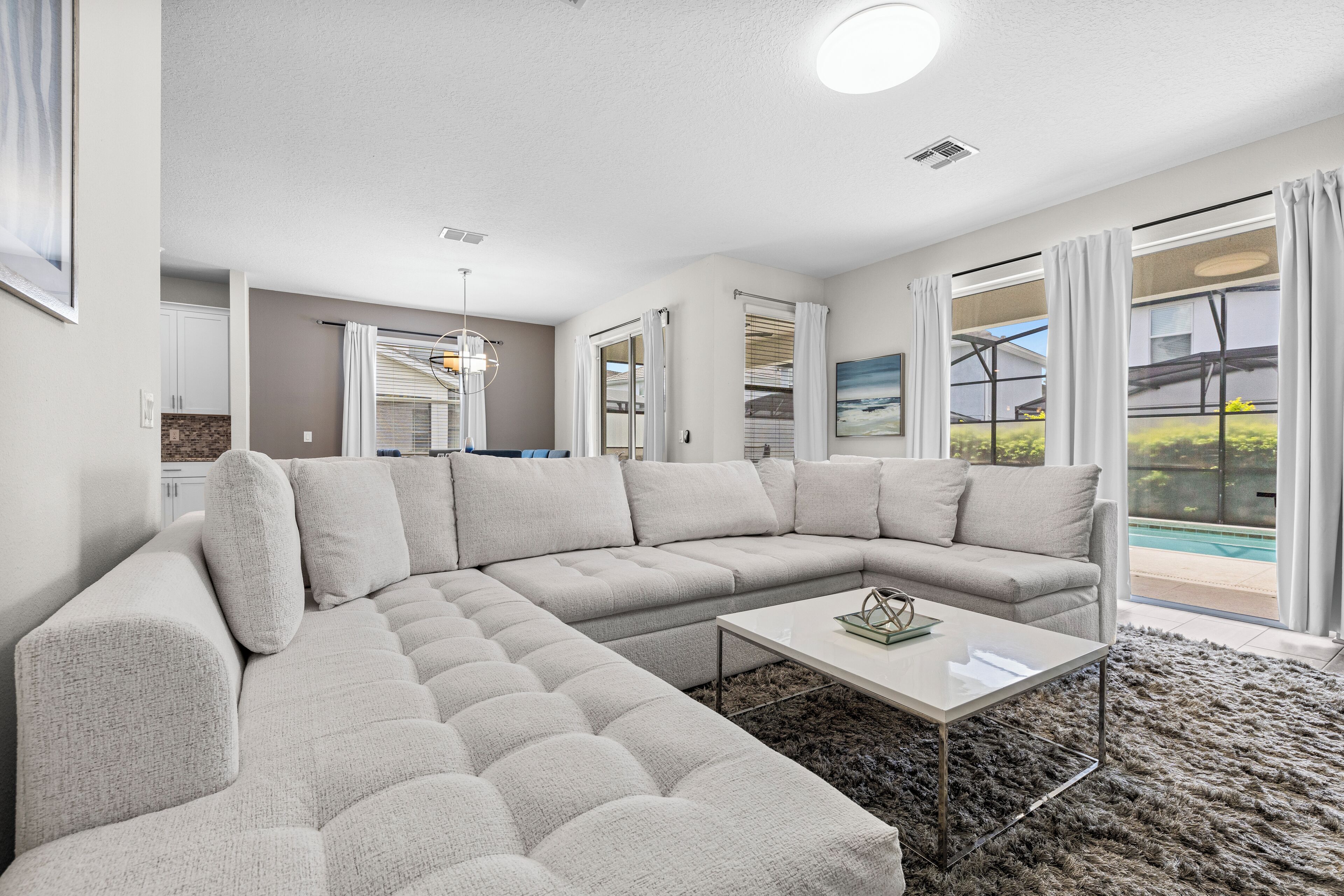 A modern living room with a sectional sofa, a coffee table, and a view of a swimming pool through large windows.
