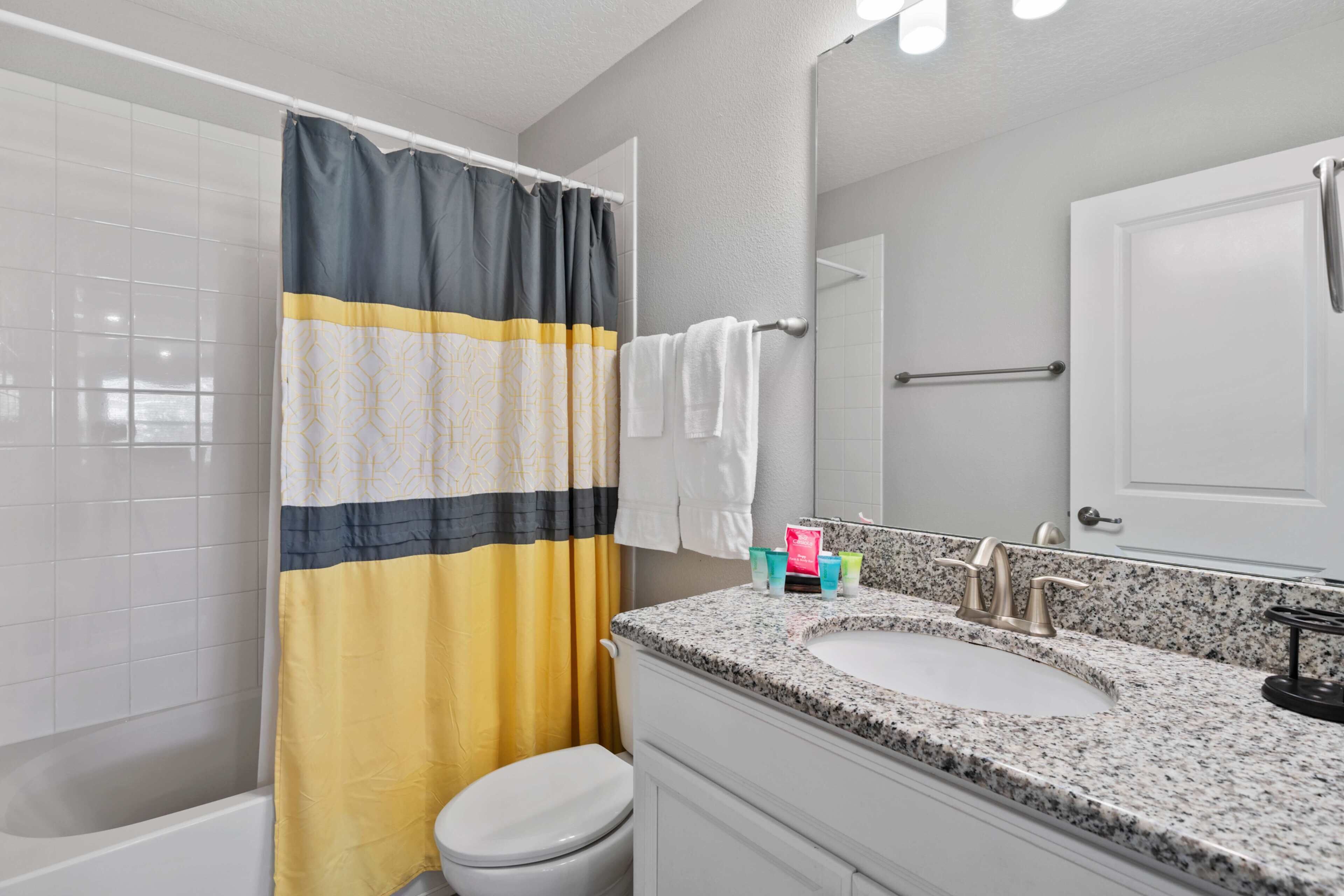 A bathroom with a shower curtain, a toilet, a sink with a faucet, and a mirror.