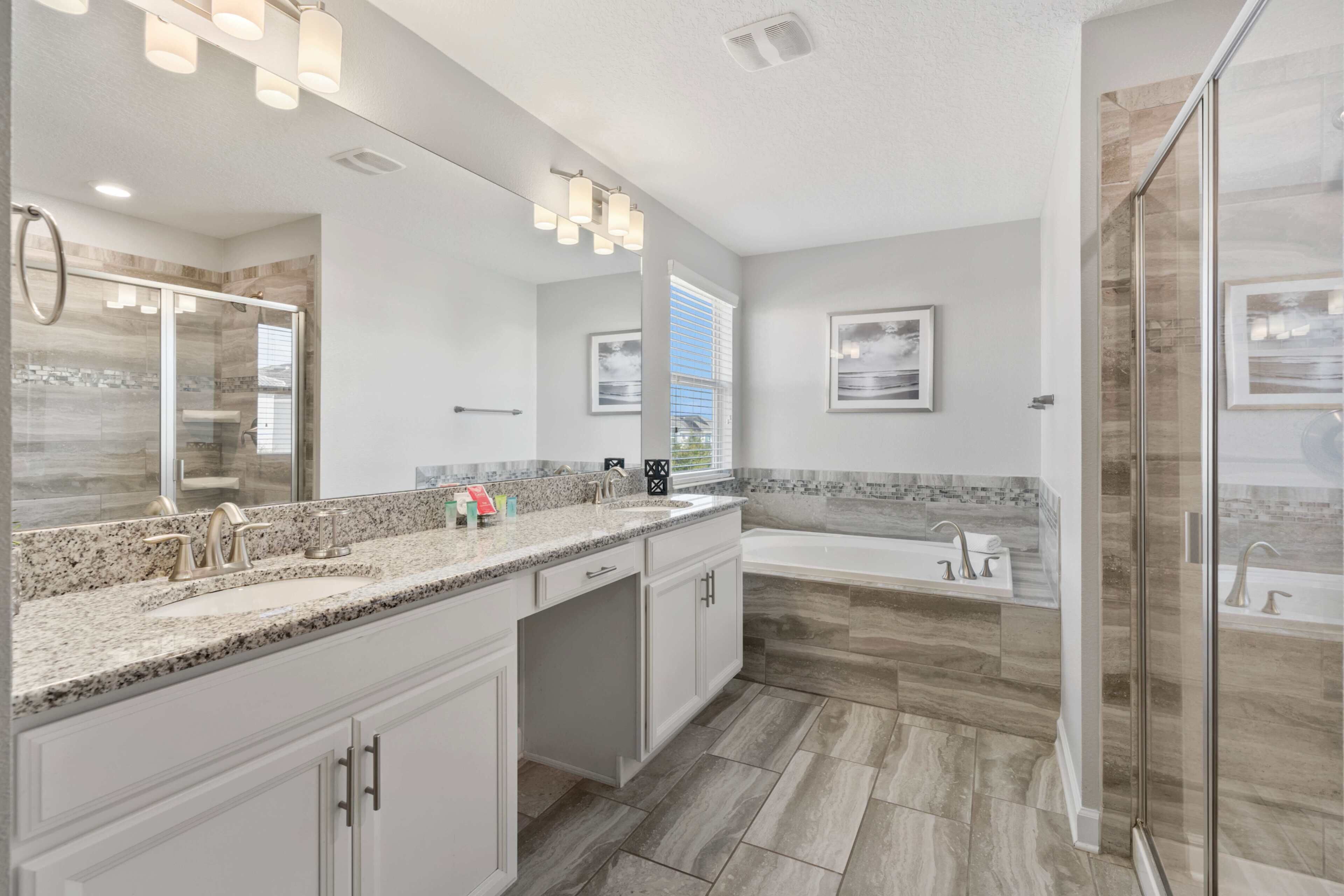 Un baño moderno con un espejo grande, encimera de granito, bañera y zona de ducha.