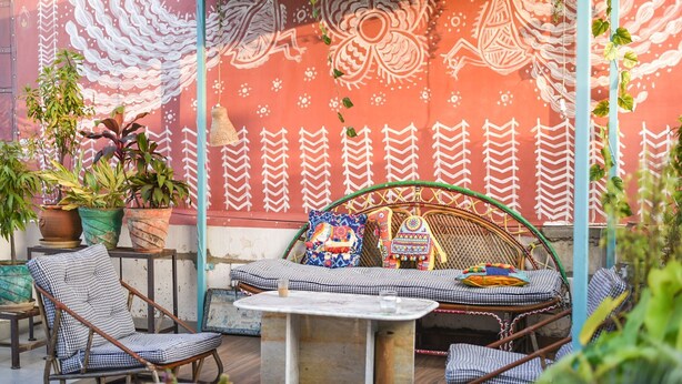 Una zona relax all'aperto accogliente, con divano e poltrone, circondata da piante in vaso e un muro decorativo.