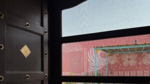 Vista attraverso una finestra che mostra una porta decorativa, un muro con motivo e posti a sedere all'aperto.