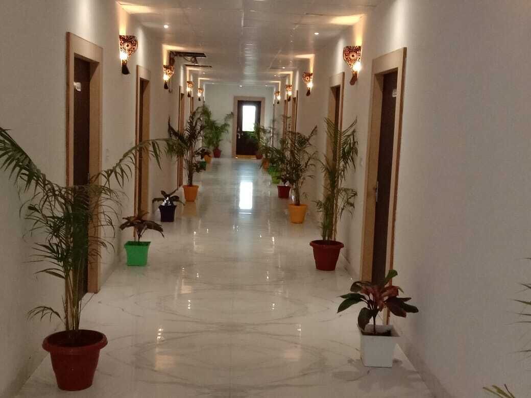 Un corridoio d'hotel con pavimento in marmo lucidato, piante in vaso e lampade a parete.