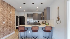 Una cocina moderna con una pared de ladrillo decorativa, tres taburetes de bar y una guitarra colgada.