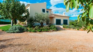 Een Mediterraan landhuis met een grindpad, een grote boom en verzorgd groen.