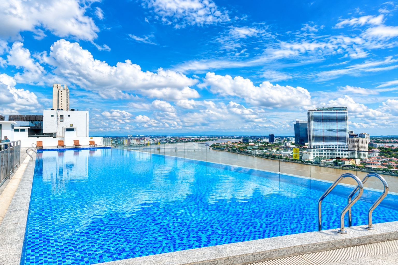 En swimmingpool med klart, blåt vand, omgivet af en by med moderne bygninger og en blå himmel.