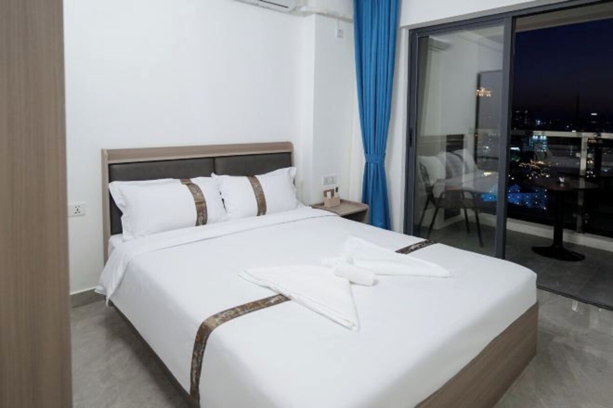 A hotel room with a large bed, a nightstand, a chair, and a view of the city at night.