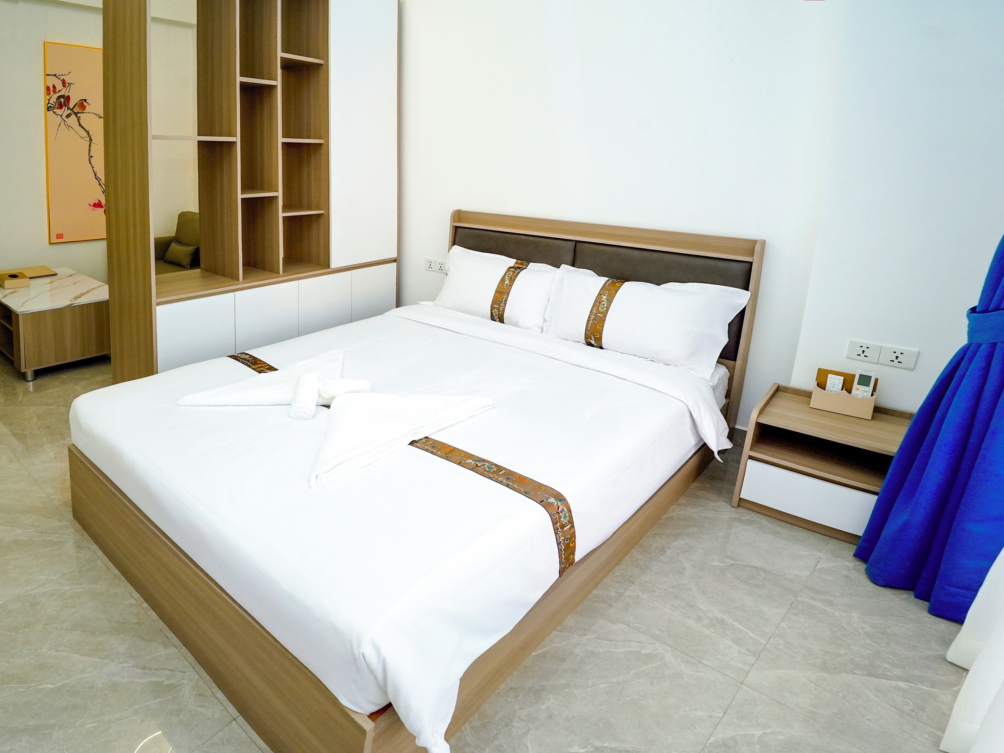 A neatly made bed with white linens and decorative pillows, a wooden nightstand with a charging station, and a large mirror with a wooden frame.