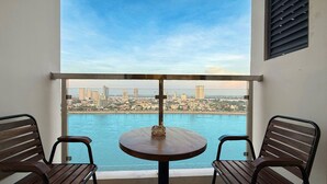 Un balcon avec une table ronde et deux chaises en bois, d’où l’on peut admirer une vue sur la ville et sur une étendue d’eau.