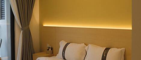 Une chambre d’hôtel avec un lit, des rideaux, un appareil de climatisation et une table de chevet avec une lampe.