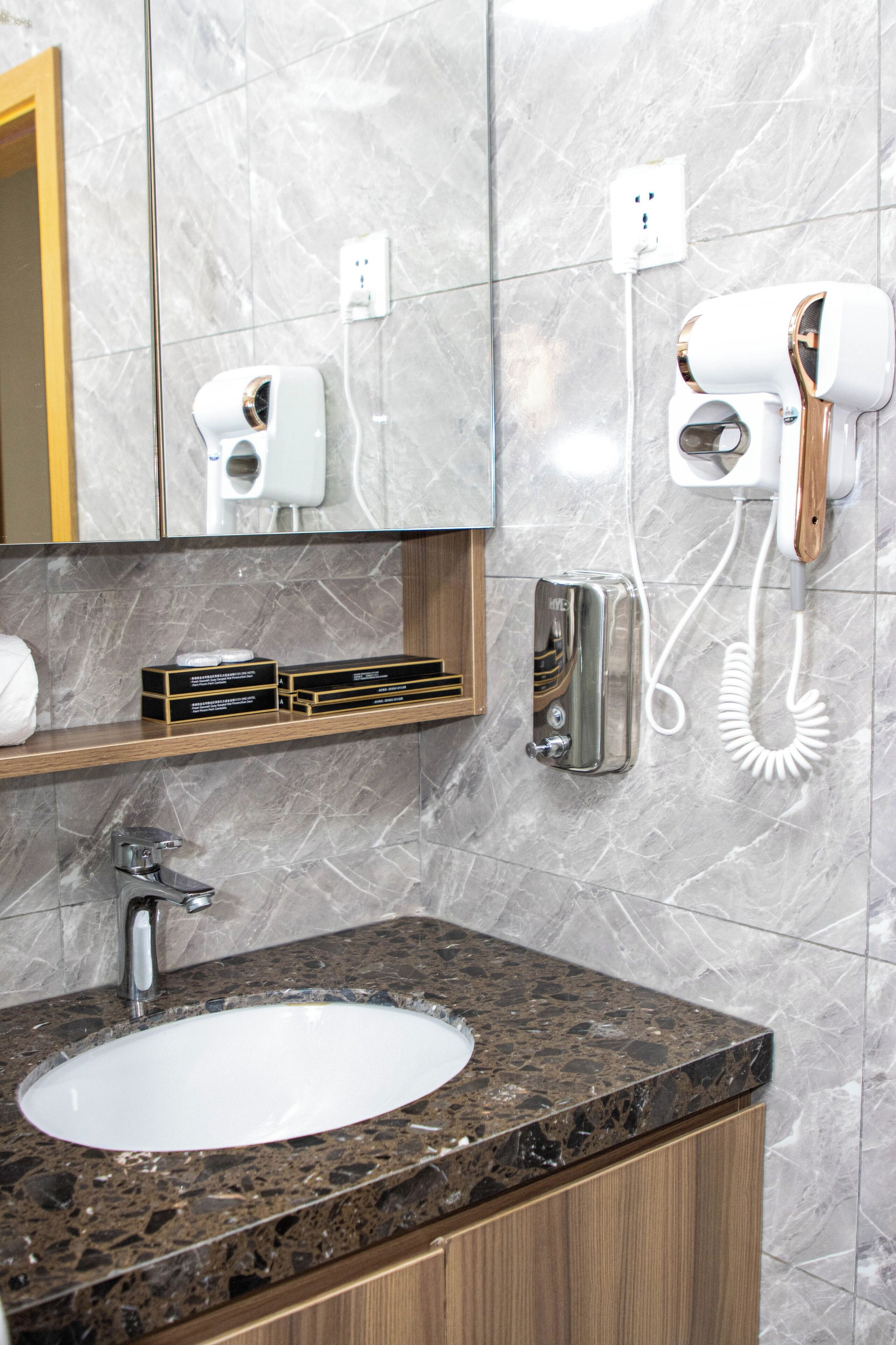 A bathroom with a marble wall, a sink with a granite countertop, a mirror, a hairdryer, and a telephone.
