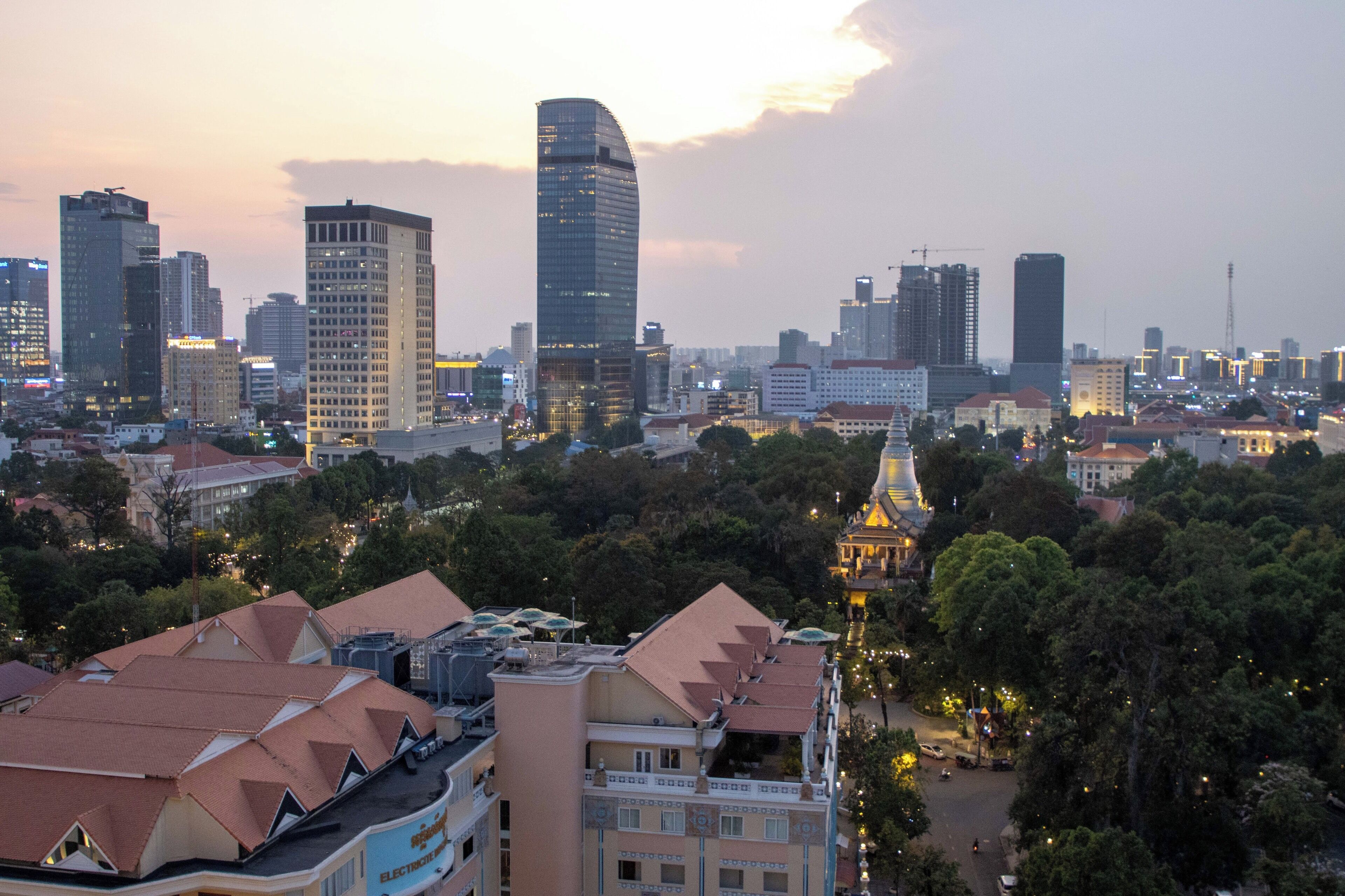 A cityscape with modern high-rise buildings, a prominent curved skyscraper, and a historic tower with a golden roof.