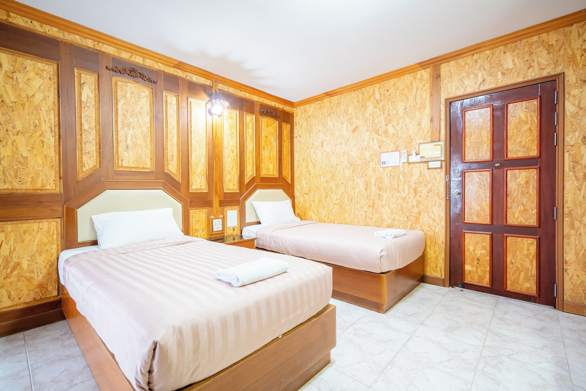 A hotel room with two beds, wooden paneling on the walls, a wooden door, and a tiled floor.