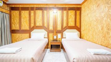 A hotel room with two beds, wooden paneling on the walls, a small wooden nightstand, and a light fixture above the nightstand.