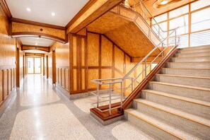 A spacious hallway with a grand staircase, polished stone floors, and wooden paneling.