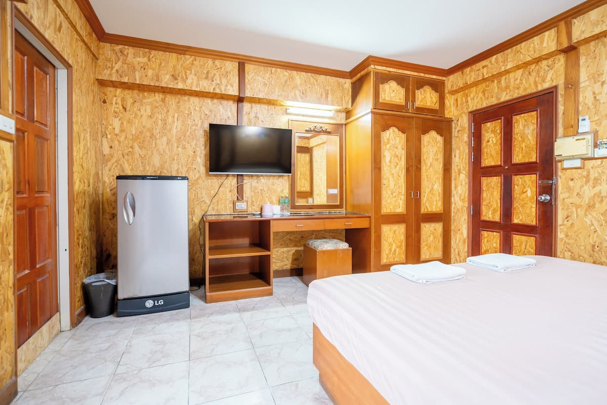 A hotel room with a bed, a desk with a flat-screen TV, a refrigerator, and wooden paneling on the walls.