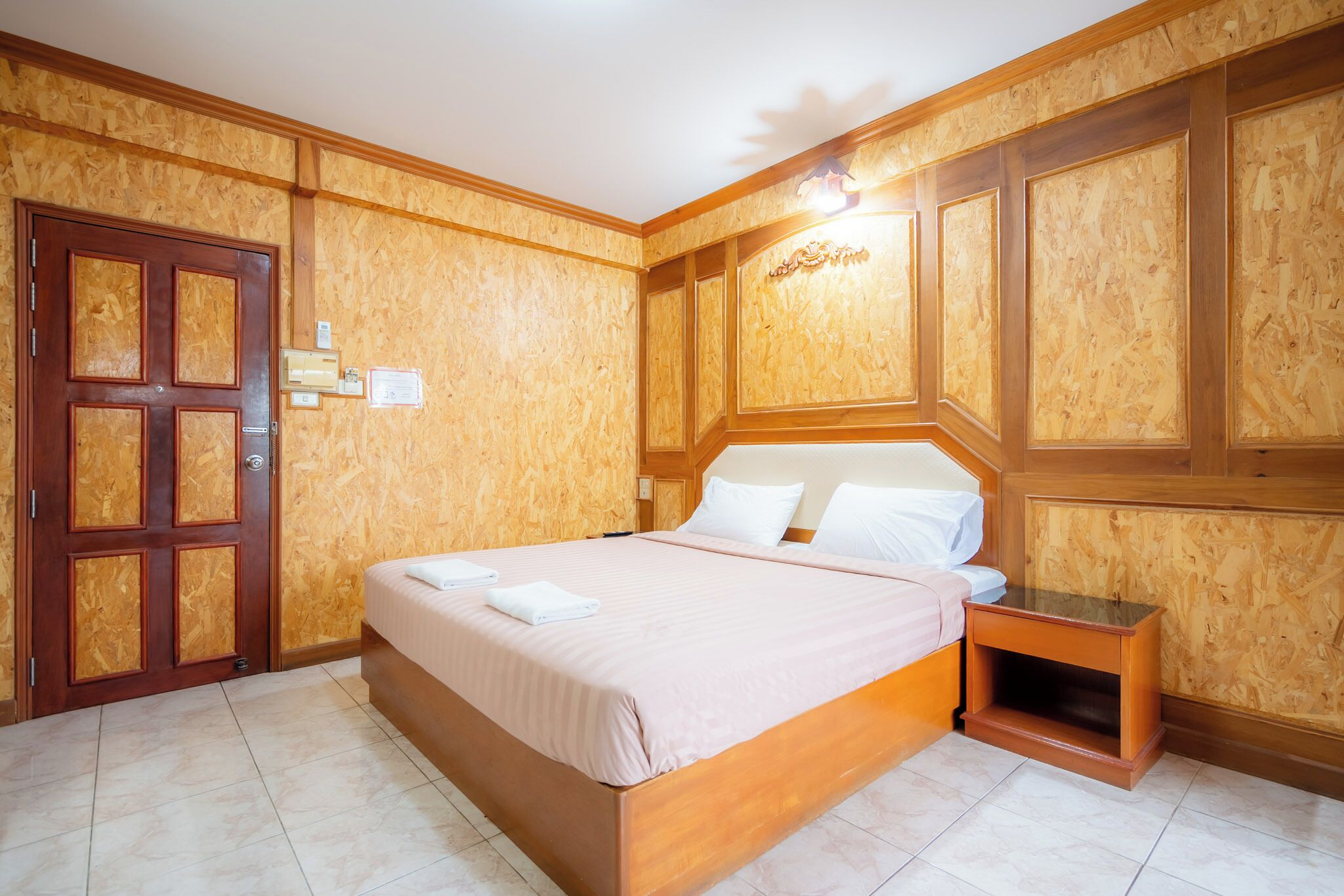 A hotel room with a wooden paneled wall, a large bed with white linens, a wooden nightstand, and a door with a lock.